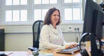 Woman in white pullover sitting at desk.